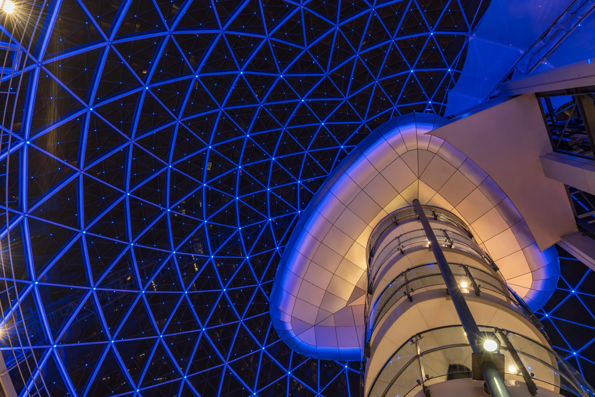 Looking up at the glass dome of Victoria Square in Belfast, showing symmetrical architecture and reflections.