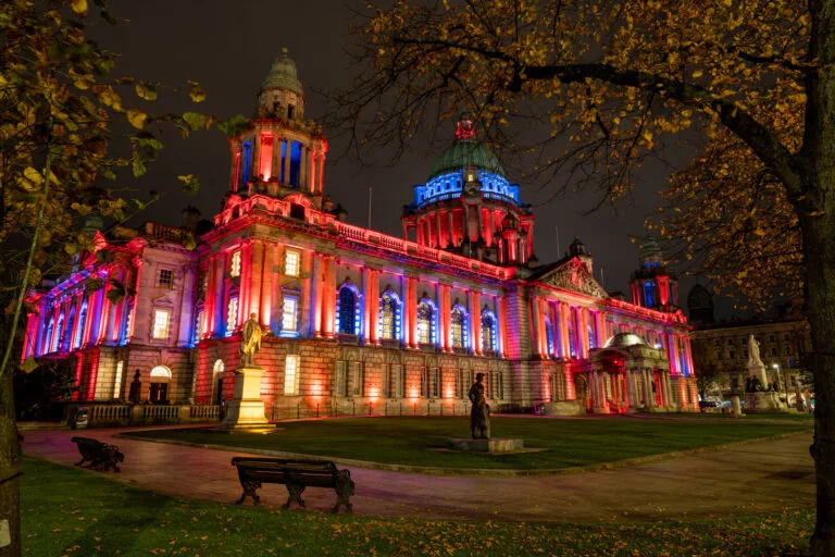 Belfast City Hall lit up in red and blue lights at night, captured with long exposure photography.