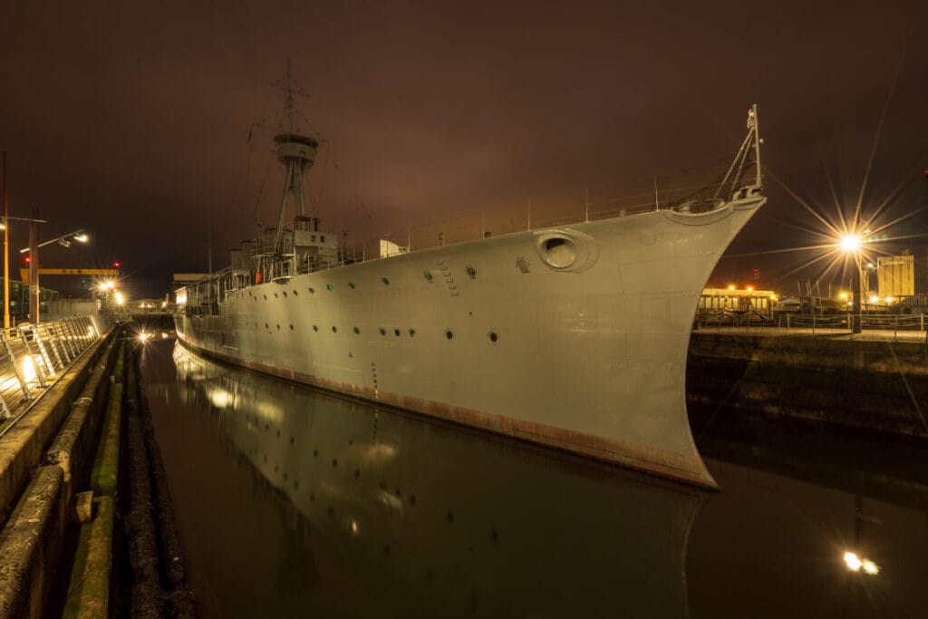 HMS Caroline in Belfast captured with 10-second long exposure at night, highlighting reflections and historic details.